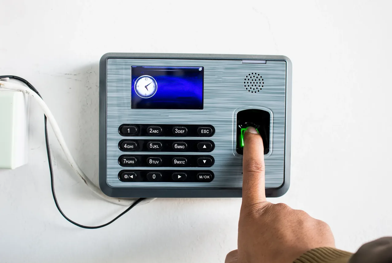 Employee pressing a finger onto a wall-mounted biometric time and attendance terminal showing a clock display